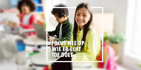 Drie leerlingen in een klasje in de lagere school. Focus op een meisje dat in de lens kijkt. De leerlingen zitten elk aan een tafeltje met hun laptop. Tekst op beeld is 'Focus mee op wie er echt toe doet'.