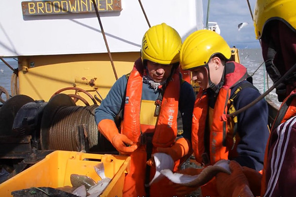 leraar en leerling bekijken gevangen vis op een boot