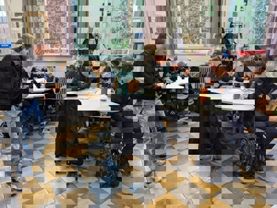 Een cameraman filmt in een klaslokaal waar leerlingen in groepjes aan een project werken