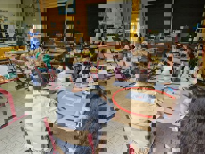 Leerlingen volgen in groepjes les in een klaslokaal met een vrouwelijke leraar vooraan