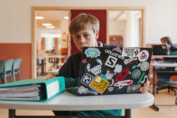 Jongen In Klas Kijkt Van Achter Zijn Laptop Recht In Camera Rh