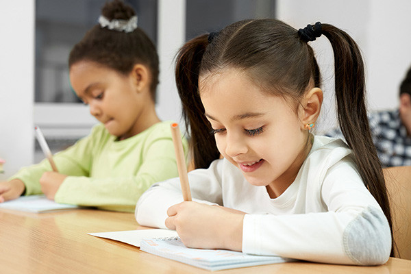 twee jonge meisjes aan een lessenaar schrijven met potlood in een schrift